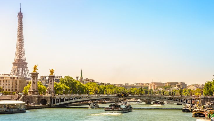 Der Eiffelturm in Paris, majestätisch vor einem strahlend blauen Himmel bei Sonnenuntergang. Die Stadt erstreckt sich im Hintergrund, und die Szene ist romantisch.