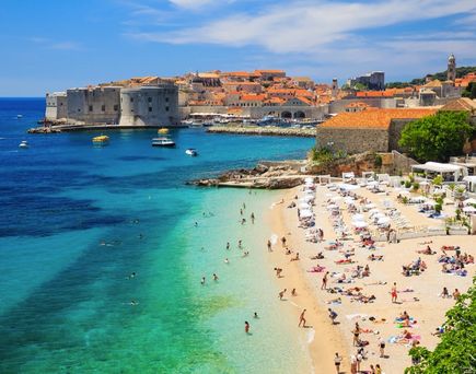 Ein belebter Sandstrand mit vielen Menschen und türkisfarbenem Wasser.