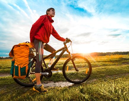 Eine Frau fährt mit einem Fahrrad auf einem Feldweg bei Sonnenuntergang, warmes Licht.