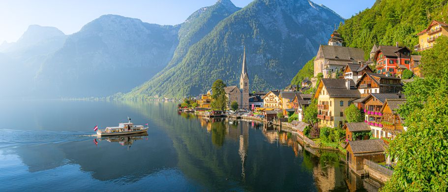 Klassischer Panoramablick auf die berühmte Altstadt von Hallstatt und den tiefblauen Alpensee mit Touristenschiff im malerischen goldenen Morgenlicht an einem wunderschönen sonnigen Tag bei Sonnenaufgang im Sommer, Salzkammergut, Österreich
