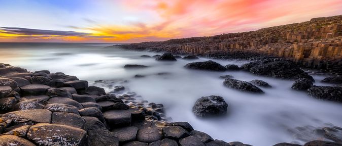 Die Basaltsäulen des Giant's Causeway bei Sonnenuntergang, mit dem Meer im Hintergrund.