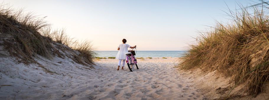 Ein Sandstrand mit Dünen und einer Person, die sich auf einem Fahrrad nähert.