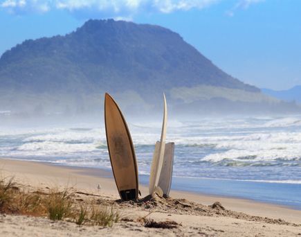 Ein historisches Holz-Surfbrett mit einem langen, schlanken Design, das auf einem sandigen Strand liegt.