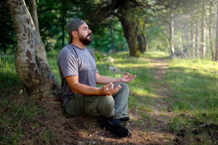Ein Mann meditiert im Wald. Bei dieser Praxis, die manchmal auch als „Waldbaden“ oder Waldmeditation bezeichnet wird, geht es darum, sich mit der Natur zu verbinden, um Ruhe zu finden, Stress abzubauen und die Achtsamkeit zu steigern.