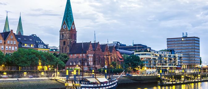 Abendstimmung am Weserufer in Bremen mit der St. Martini Kirche, historischen Gebäuden und einem Segelschiff im Vordergrund.