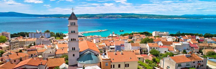 Eine Stadtansicht von Crikvenica mit roten Dächern und Blick auf das Meer und einen Kirchturm.