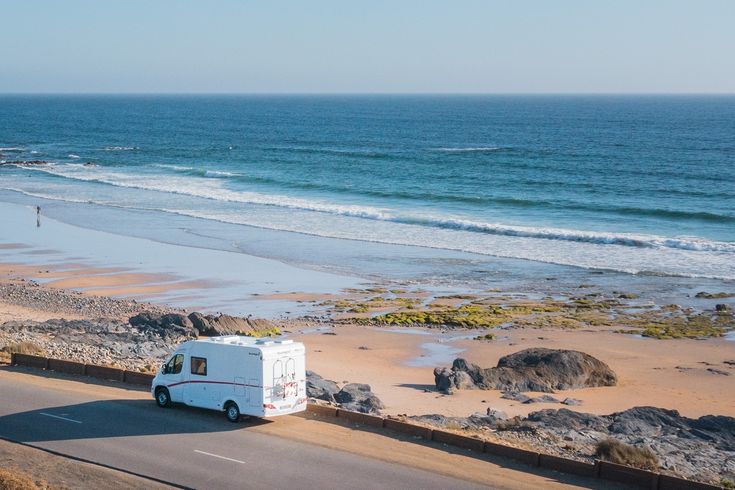 Camper fährt entlang einer Straße am Strand mit hellblauem Meer in Portugal 