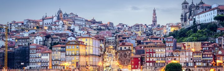 Die beleuchtete Skyline von Porto, Portugal, bei Sonnenuntergang, mit Gebäuden am Fluss.