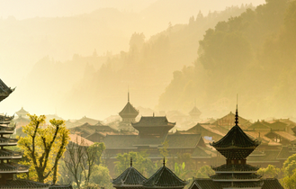 Eine alte chinesische Landschaft mit traditioneller Architektur, die sich in einer gebirgigen Kulisse mit Nebel und üppiger Vegetation befindet.
