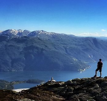 Eine Person steht auf einem Bergkamm und blickt über eine weite, bergige Landschaft in Norwegen.