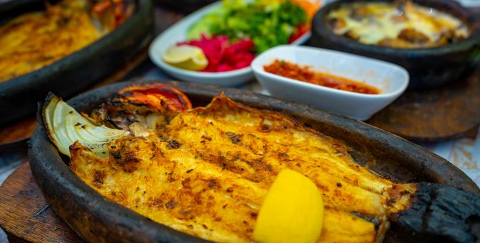 kleine schwarze Essenschalen aus Eisen mit lecker angerichteten Gerichten wie gebratenem Fisch, Kartoffeln, Tomaten und Paprika