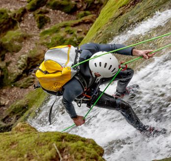 Ein Mann klettert an einer Felswand, während Wasser unter ihm lang fließt.