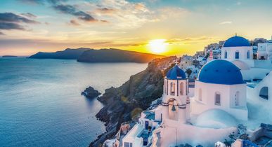Santorin. Weiß-blaue Häuser im Hang, davor das türkisfarbene Meer. Ansicht bei Sonnenuntergang.