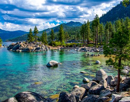 Ein See mit türkisfarbenem Wasser, umgeben von grünen Bäumen und Bergen.