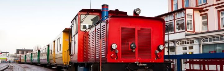 Kleinbahn Borkum. Roter Zug fährt durch die Stadt.
