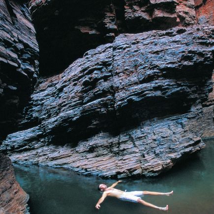 Camper Australien Urlaub Reisen Mann schwimmt im Wasser zwischen Felsen Karijini Nationalpark