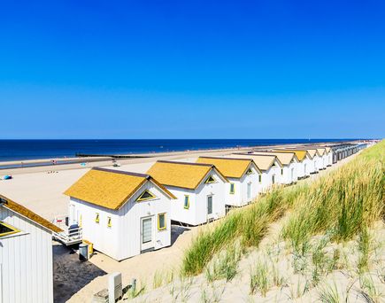 Ein Sandstrand mit kleinen weißen Strandhäusern und einem blauen Himmel.