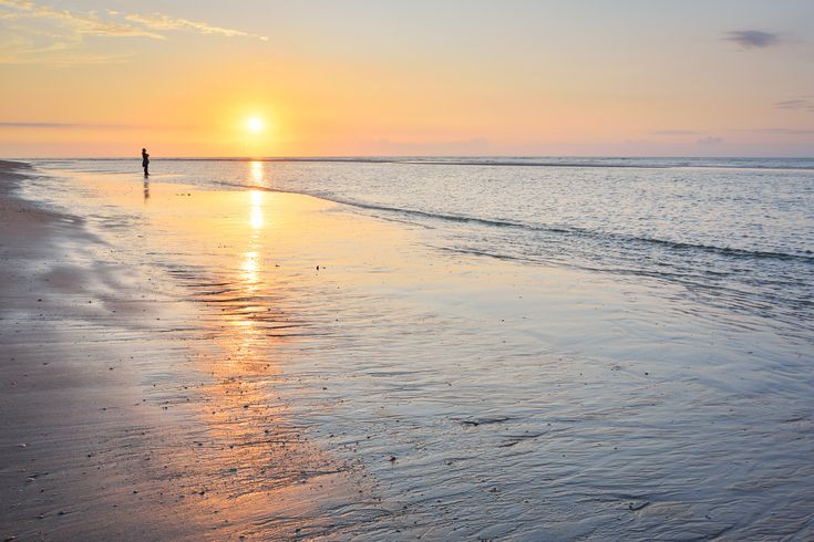 Sonnenuntergang am Strand. Ein Mann spaziert den Flutsaum lang.