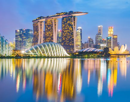 Beleuchtete Skyline von Singapur spiegelt sich im Wasser der Marina Bay – Die moderne Architektur Singapurs erstrahlt in der Dämmerung in farbenfroher Spiegelung auf der Wasseroberfläche.