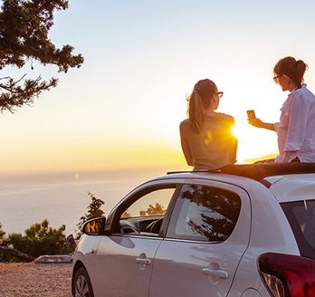 Paar sitzt auf einem Auto mit Sonnenuntergang im Hintergrund