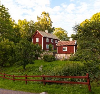 Traditionelles rotes schwedisches Haus mit weißen Fensterrahmen und grünem Garten.