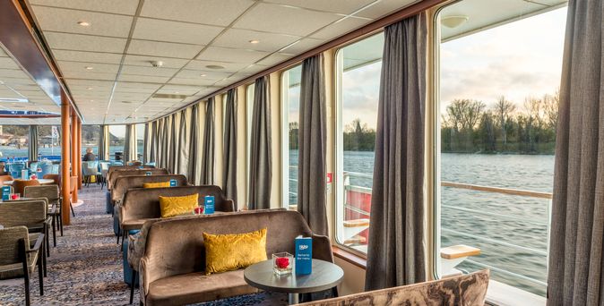 Ein Panorama-Salon auf einem Schiff mit bequemen Sesseln und großen Fenstern.