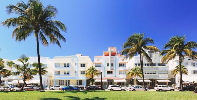 Ocean Drive in Miami Beach, Florida, mit seinen ikonischen Art-déco-Hotels und dem belebten Strandbereich, der sich unter einem klaren blauen Himmel erstreckt.