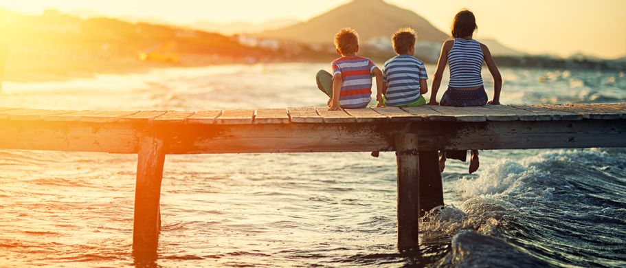Kinder sitzen auf einem Steg am Meer bei Sonnenuntergang
