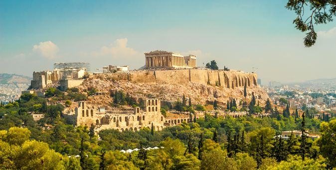 Blick über grüne Vegetation auf die Akropolis von Athen, im Hintergrund blauer Himmel