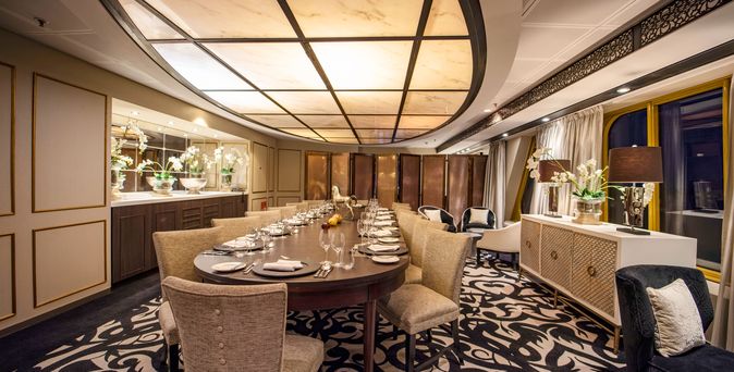 Ein elegantes Restaurant auf einem Schiff mit einem langen Tisch und Stühlen.