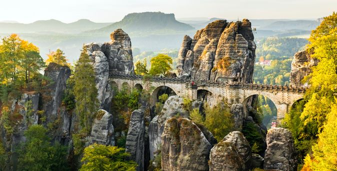 Eine beeindruckende Ansicht der Basteibrücke in der Sächsischen Schweiz, die sich zwischen hoch aufragenden Felsformationen erstreckt und einen weiten Blick über den Nationalpark Sächsische Schweiz bietet.