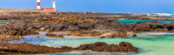 Leuchtturm hinter den Felsen und dem Meer.