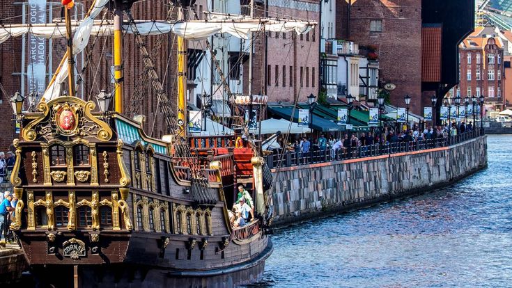 Ein historischer Kran oder eine Hebevorrichtung am Hafen, umgeben von Gebäuden.