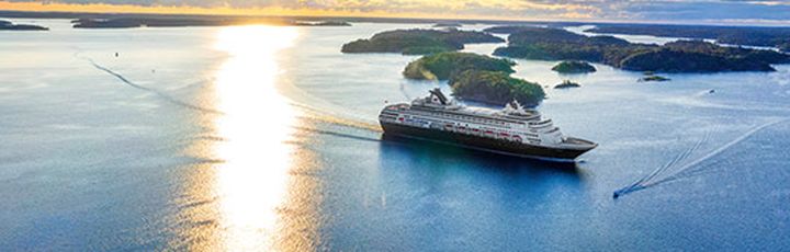 Ein Kreuzfahrtschiff auf dem Wasser mit einer Stadtansicht im Hintergrund.