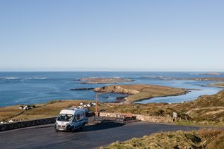 Eine kurvenreiche Küstenstraße, die Sky Road in Clifden, County Galway, Irland, schlängelt sich entlang der zerklüfteten Küste und bietet weite Ausblicke auf das Meer und die grüne Landschaft.