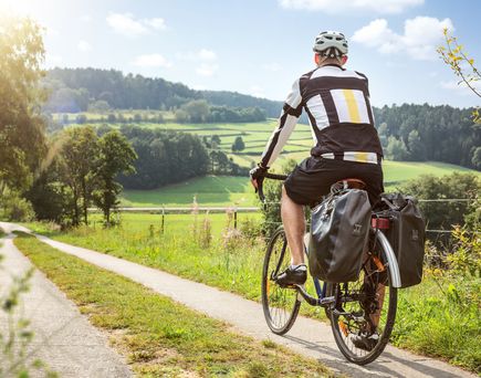 Ein Fahrradfahrer fährt auf einem Radweg durch eine grüne Landschaft bei Sonnenuntergang.