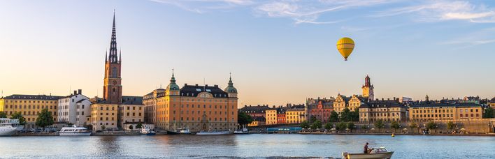 Blick auf die Silhouette von Riddarholmen gegen das Wasser, ein gelber Heißluftballon schwebt über den Gebäuden, Boot fährt vorbei, Stockholm, Schweden