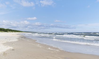 Ein breiter Sandstrand an der Ostsee mit Wellen, Dünengras und einem bewölkten Himmel, in Damp, Deutschland.