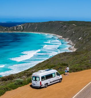 Parkender Camper an einer Parkbucht oberhalb einer Meereinbuchtung. Mann und Frau schauen auf das Meer und halten sich in den Armen. In Australien  