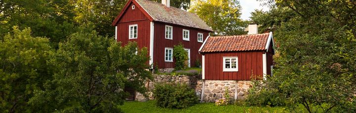 Traditionelles rotes schwedisches Haus mit weißen Fensterrahmen und grünem Garten.
