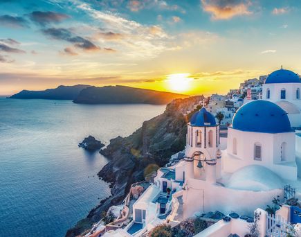 Santorin. Weiß-blaue Häuser im Hang, davor das türkisfarbene Meer. Ansicht bei Sonnenuntergang.