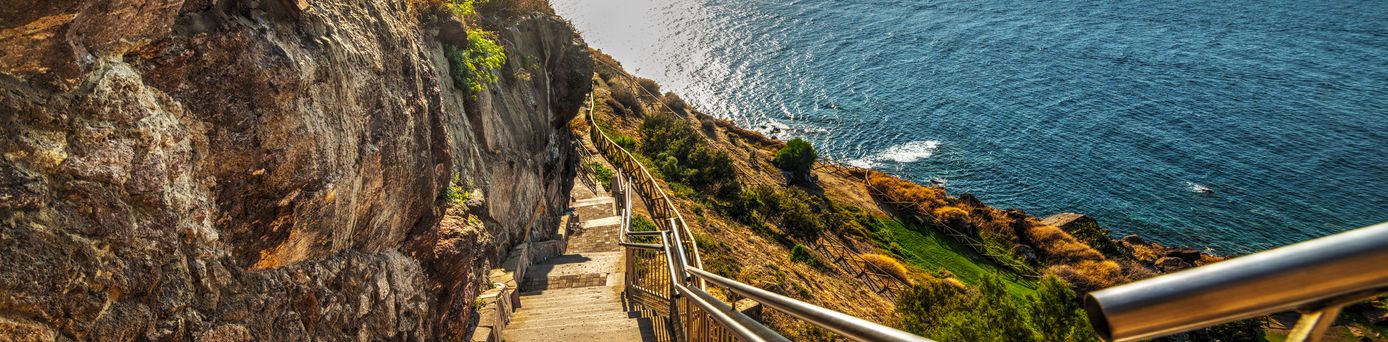 Eine spektakuläre Felsformation an der Küste Sardiniens, Italien, zeigt eine Höhle, die Grotta di Nettuno, und eine Treppe, die zur Meeresoberfläche führt, mit dem tiefblauen Mittelmeer im Hintergrund.