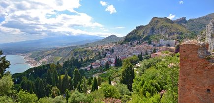 Eine Panoramablick auf die Stadt Taormina, eingebettet in eine grüne Hügellandschaft mit Blick auf das Meer.
