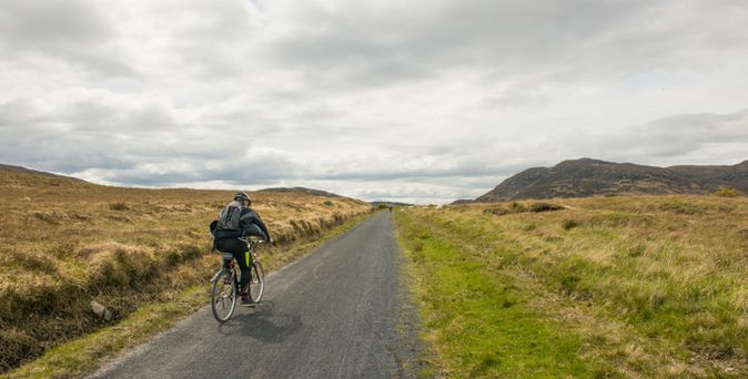 Eine Person geht auf einem Feldweg, umgeben von grüner Landschaft.
