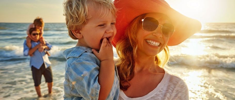 Eine Frau hält ein Kind im Arm am Strand.