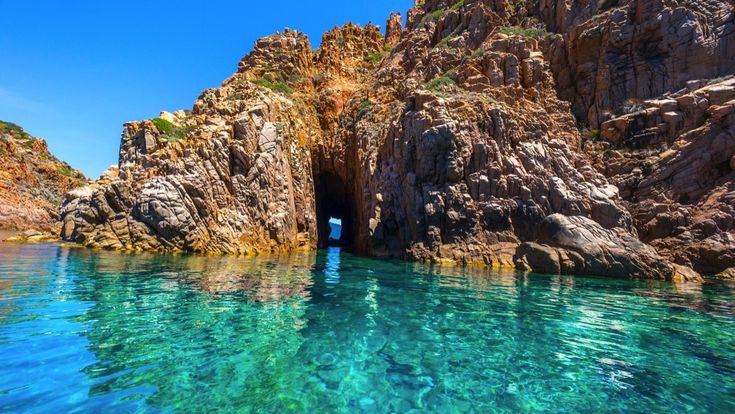 Die beeindruckenden roten Felsformationen der Calanques de Piana in Korsika, Frankreich, die steil aus dem türkisblauen Meer aufragen, umgeben von üppiger Vegetation.