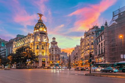 Die Gran Vía in Madrid bei Sonnenuntergang, mit dem beleuchteten Gebäuden.