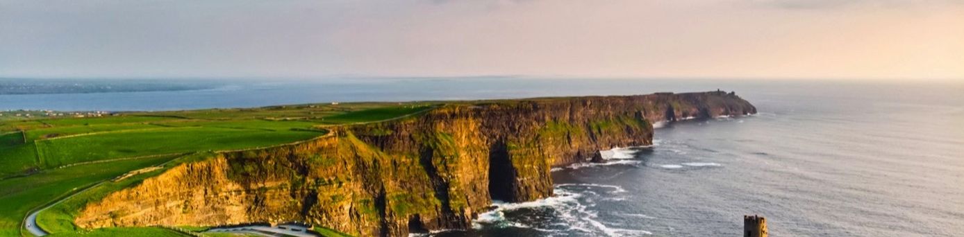 Die imposanten Cliffs of Moher in der Grafschaft Clare, Irland, erheben sich dramatisch aus dem Atlantik, mit grünen Klippen und der weiten See unter einem bewölkten Himmel.