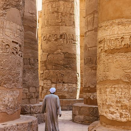Die Säulenhalle des Karnak-Tempelkomplexes, mit hoch aufragenden, reich verzierten Säulen, die ein blau bemaltes Deckengewölbe tragen.