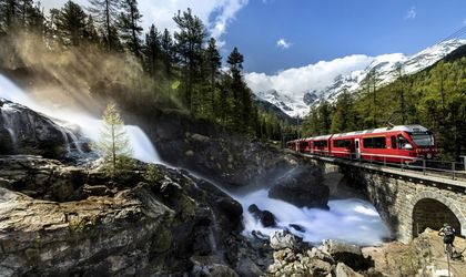Zug fährt auf einer Brücke durch eine bergige Landschaft mit grüner Natur